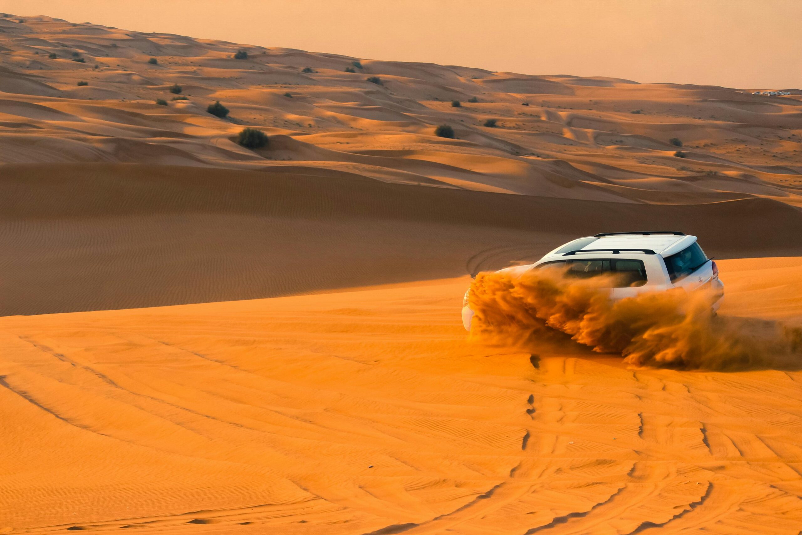 a thrilling scene of a 4x4 vehicle kicking up sand as it drives over steep sand dunes, showcasing the excitement of dune bashing in Dubai Desert. Luxury desert safari