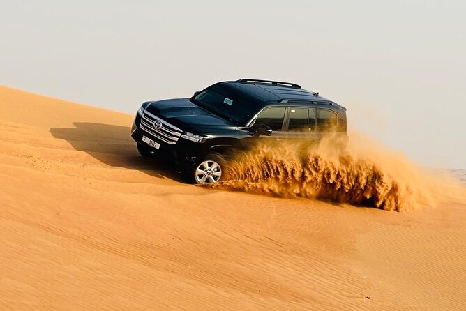 An off road vehicle kicking up a trail of send while maneuvering through towering desert dunes during a thrilling dune bashing safari